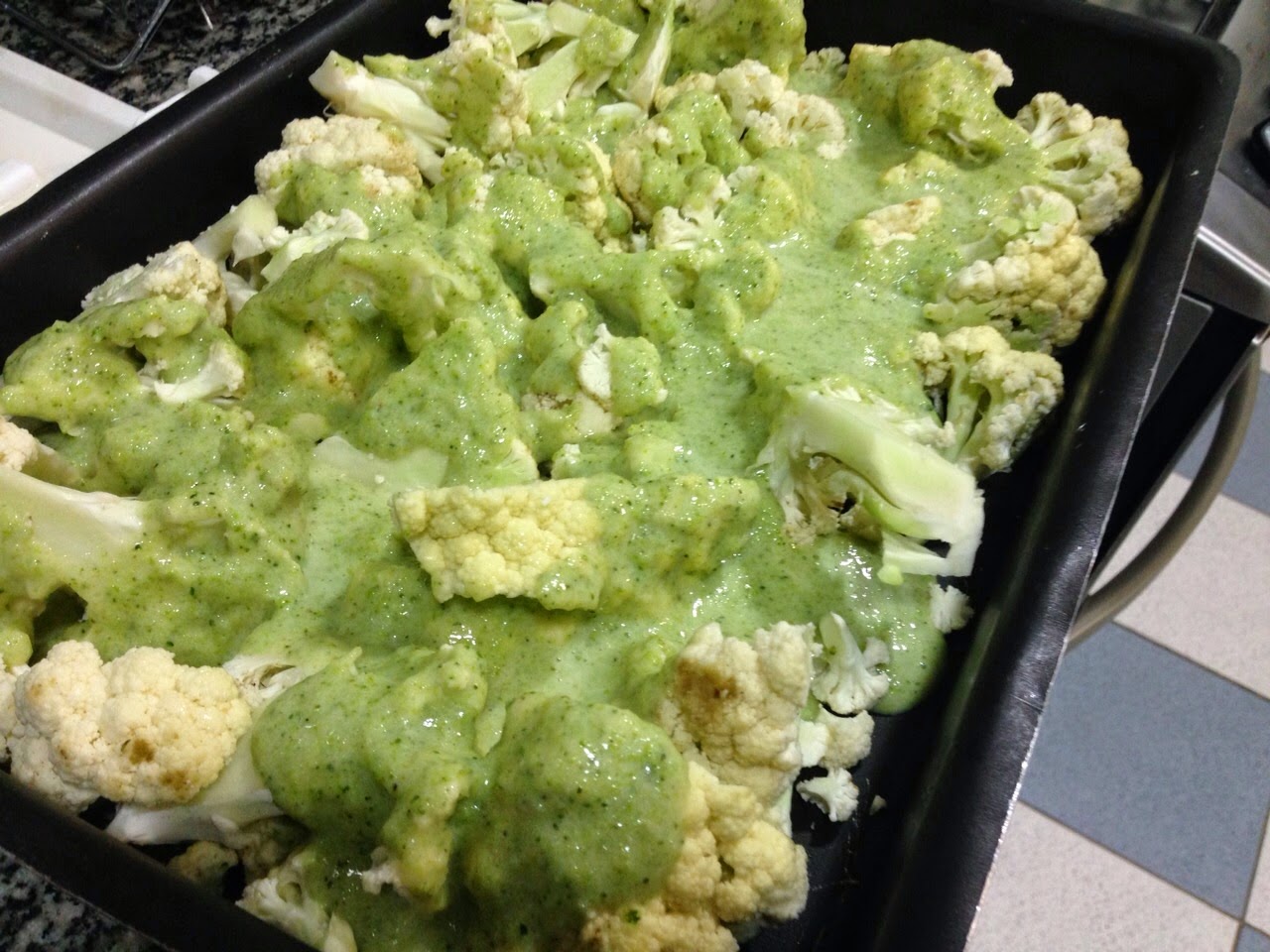 Cauliflower florets topped with a bright green sauce in a black baking tray, green and cream tones