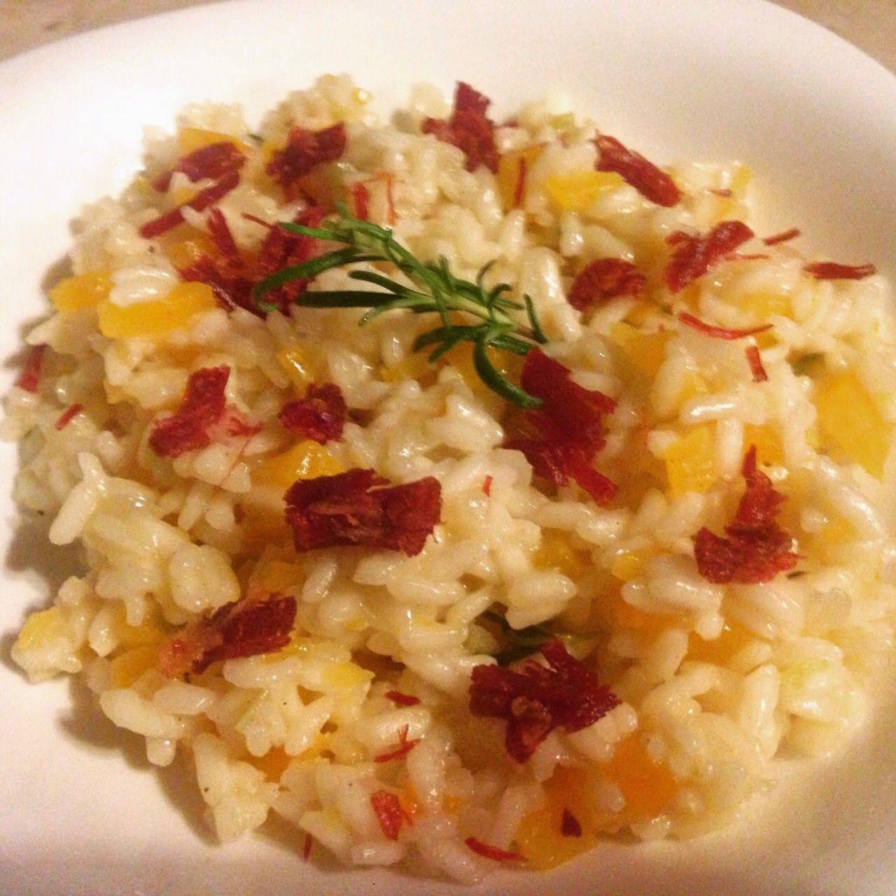 Prato de arroz cremoso guarnecido com pedaços de laranja, ervas secas e raminho de alecrim, em tons quentes de amarelo e vermelho