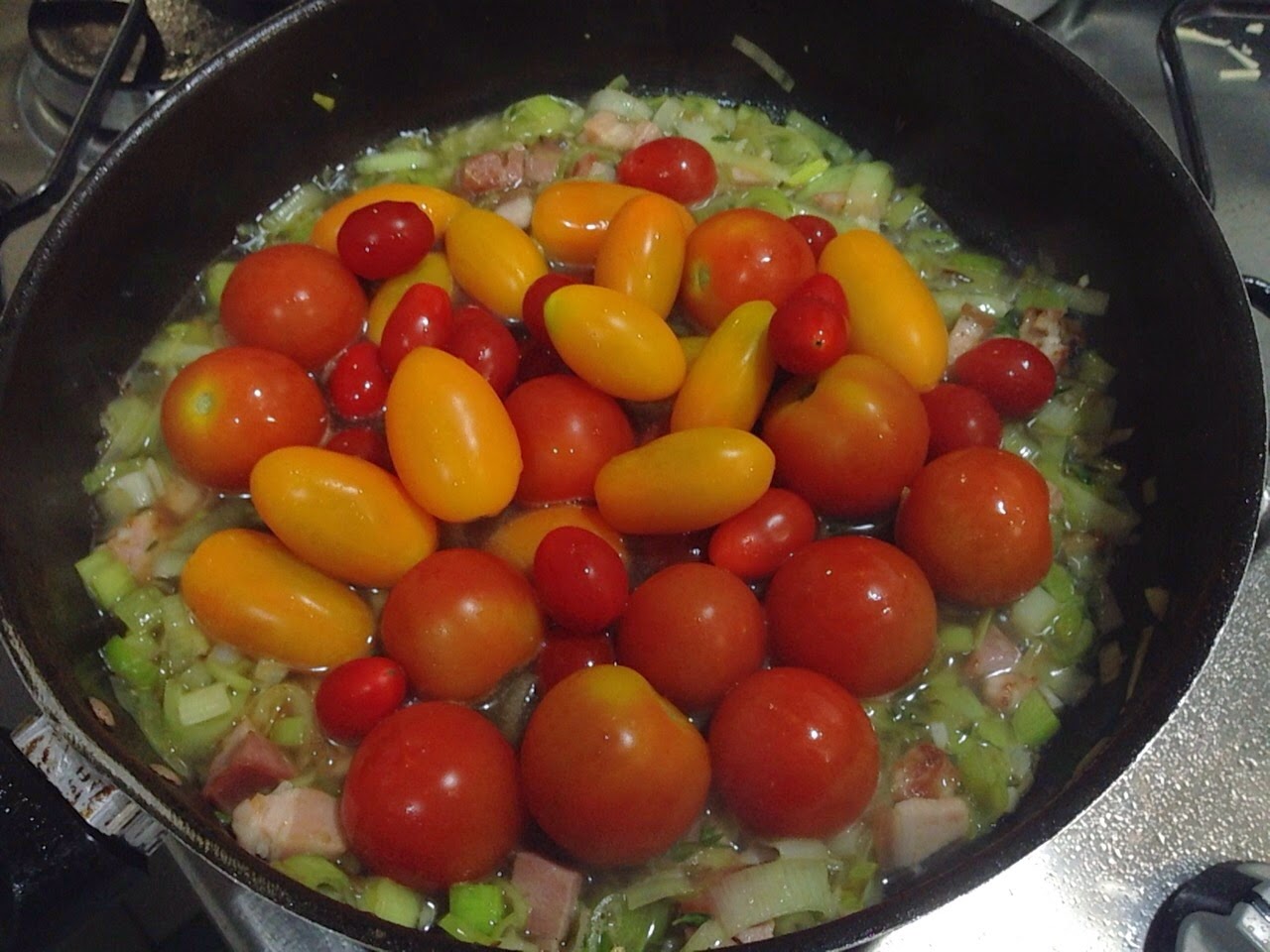 Tomates cereja vermelhos e amarelos refogando com alho-poró picado em panela preta, clima colorido e caseiro