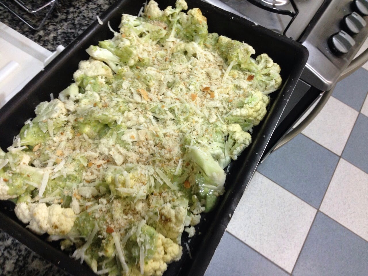 Roasted cauliflower topped with grated cheese and breadcrumbs on a baking tray, warm yellow and green tones