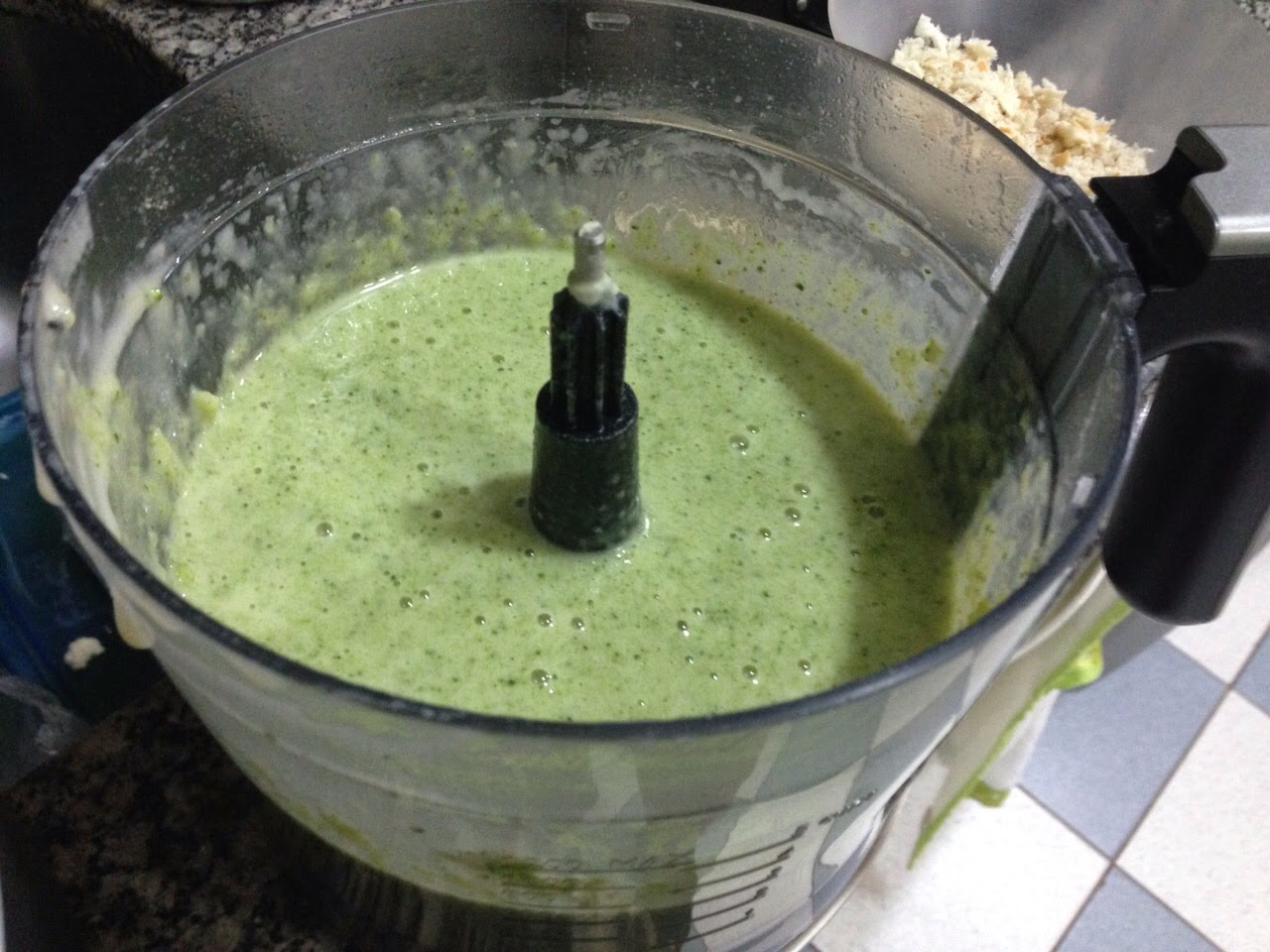 Mistura de molho verde batido dentro do copo de um processador sobre bancada de cozinha, tons verdes vibrantes e claros